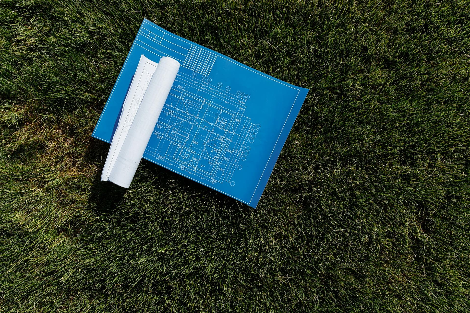 Top view of architectural blueprints on a grassy field, ideal for construction themes.